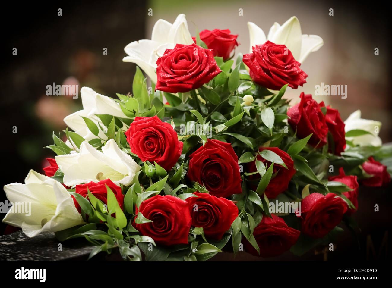Rote und weiße Beerdigungsblumen auf einem Grabstein auf einem Friedhof. Verwandte haben Gedenkblumen ins Grab gebracht. Wunderschöner Blumenstrauß zur Erinnerung Stockfotografie