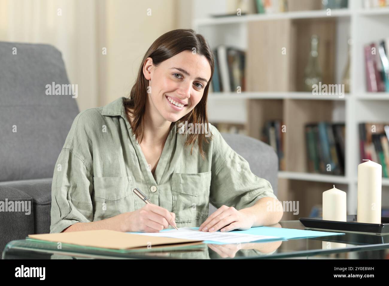 Glückliche Frau, die Verträge unterschreibt und zu Hause in die Kamera schaut Stockfoto