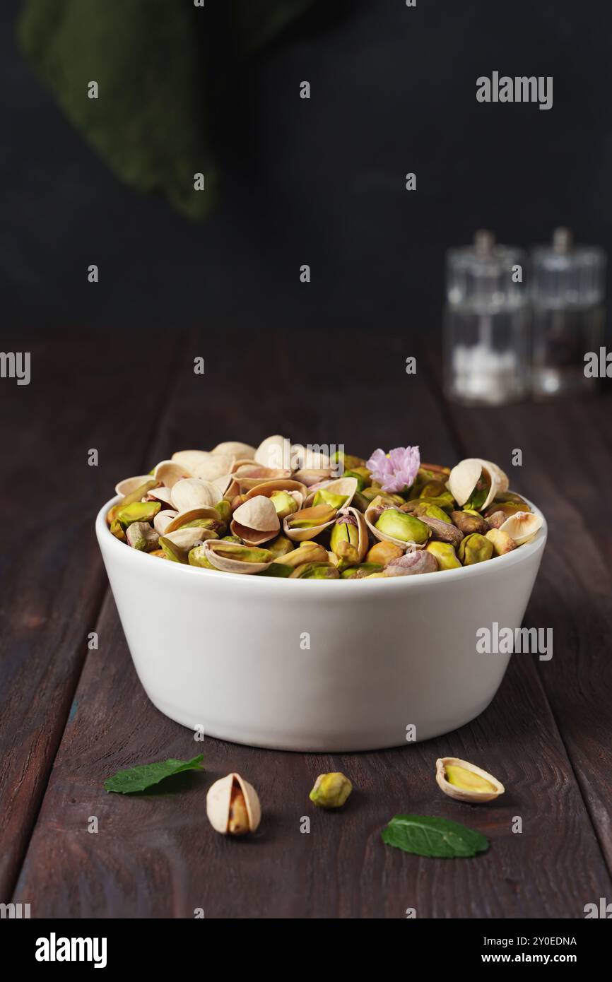 Mit und ohne Schale gefüllte weiße Schüssel mit Pistazien auf einem dunklen hölzernen rustikalen Tisch Stockfoto