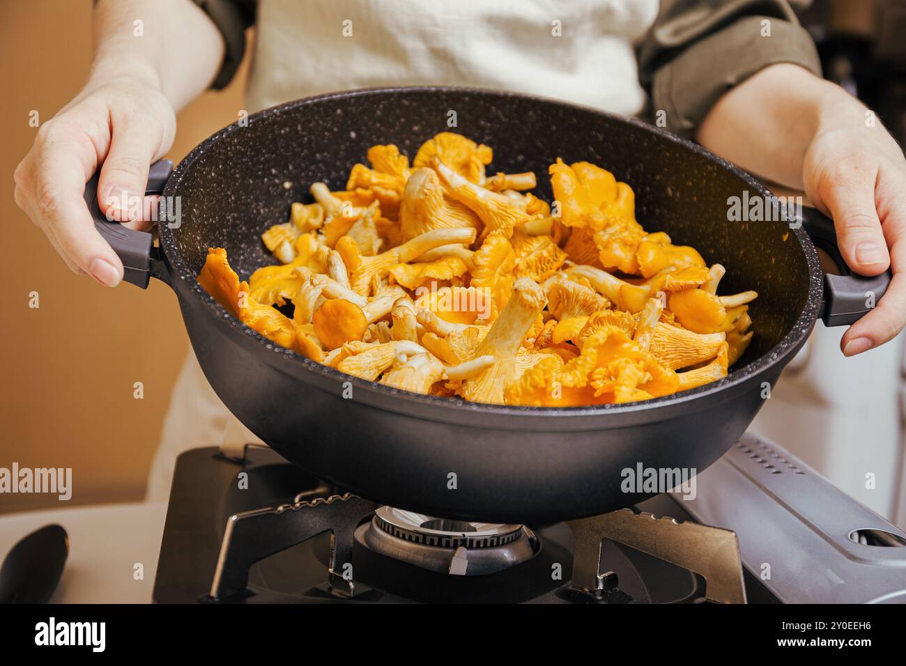 Hände halten Pfanne gefüllt mit frischen Pfifferlingen, Kochen auf Gasherd, Zubereiten gesundes vegetarisches Essen Stockfoto