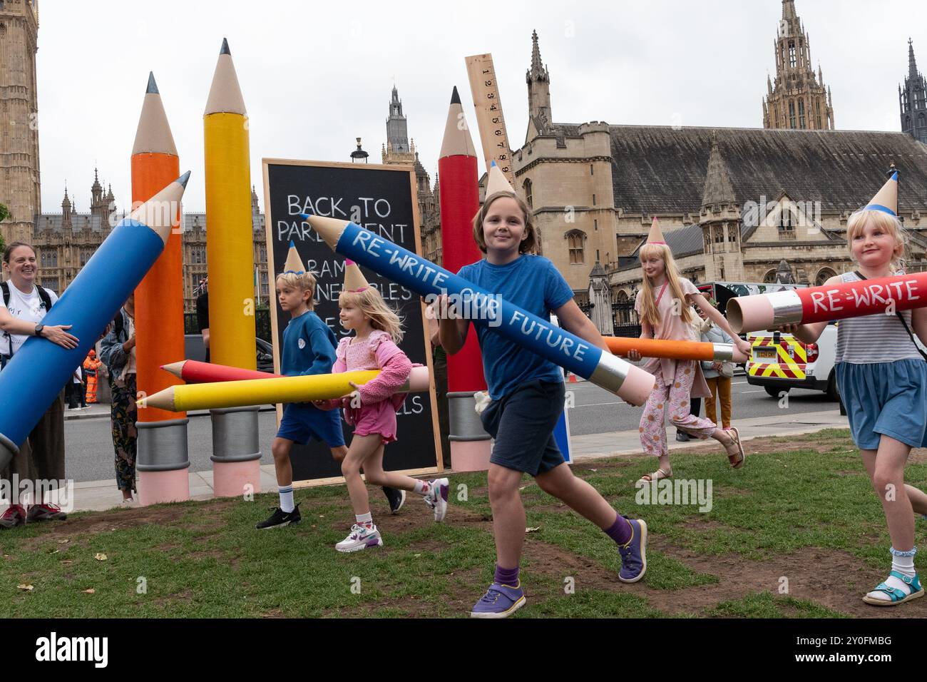 London, Großbritannien. 2. September 2024. Kinder mit riesigen Bleistiften und einer Tafel mit Botschaften an die Regierung erscheinen bei einem Theaterprotest auf dem Parliament Square, als Klimaaktivisten von Müttern die Bühne einer "zurück zur Schule, zurück zum Parlament"-Kundgebung aufsteigen. Mit der Aufforderung an die Labour-Regierung von Sir Keir Starmer, sich stärker für Maßnahmen zur Bekämpfung der globalen Wärmeentwicklung, zur Bekämpfung des Verlusts an biologischer Vielfalt und zur Senkung der Energiekosten einzusetzen, fiel die Veranstaltung zeitgleich mit der Rückkehr des Parlaments aus der Sommerpause und dem Beginn der neuen Schulzeit zusammen. Quelle: Ron Fassbender/Alamy Live News Stockfoto