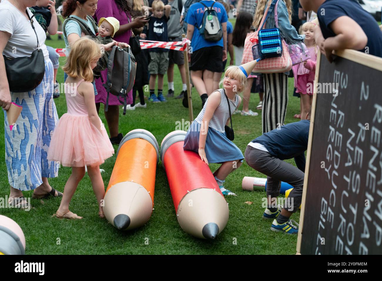 London, Großbritannien. 2. September 2024. Kinder mit riesigen Bleistiften und einer Tafel mit Botschaften an die Regierung erscheinen bei einem Theaterprotest auf dem Parliament Square, als Klimaaktivisten von Müttern die Bühne einer "zurück zur Schule, zurück zum Parlament"-Kundgebung aufsteigen. Mit der Aufforderung an die Labour-Regierung von Sir Keir Starmer, sich stärker für Maßnahmen zur Bekämpfung der globalen Wärmeentwicklung, zur Bekämpfung des Verlusts an biologischer Vielfalt und zur Senkung der Energiekosten einzusetzen, fiel die Veranstaltung zeitgleich mit der Rückkehr des Parlaments aus der Sommerpause und dem Beginn der neuen Schulzeit zusammen. Quelle: Ron Fassbender/Alamy Live News Stockfoto