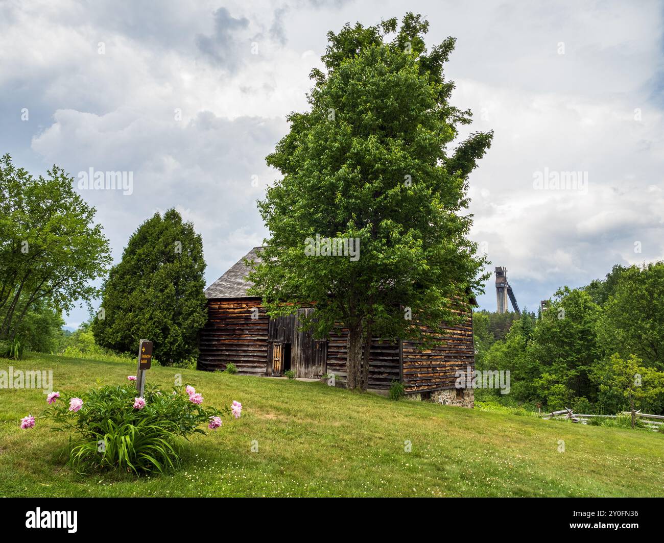Eine bezaubernde Holzscheune auf der John Brown Farm, eingerahmt von leuchtenden Blumen und vor dem Hintergrund des berühmten Olympischen Skisprungturms. Stockfoto