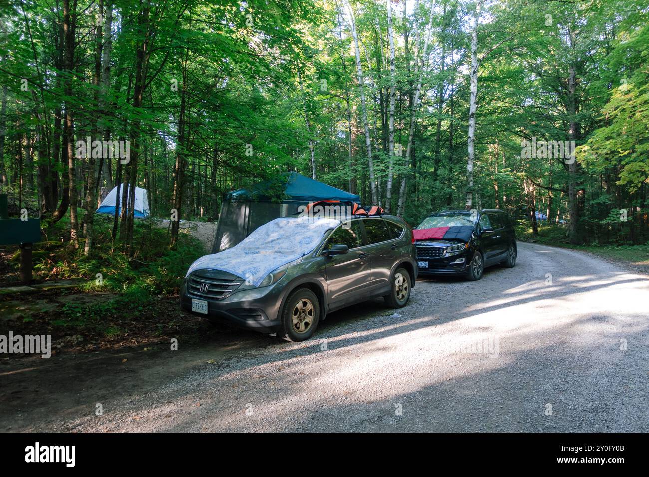 Autos, die auf der Straße eines Campingplatzes geparkt sind, mit Handtüchern, die zum Trocknen ausgelegt sind, spiegeln eine lässige Umgebung des Campingplatzes wider. Stockfoto