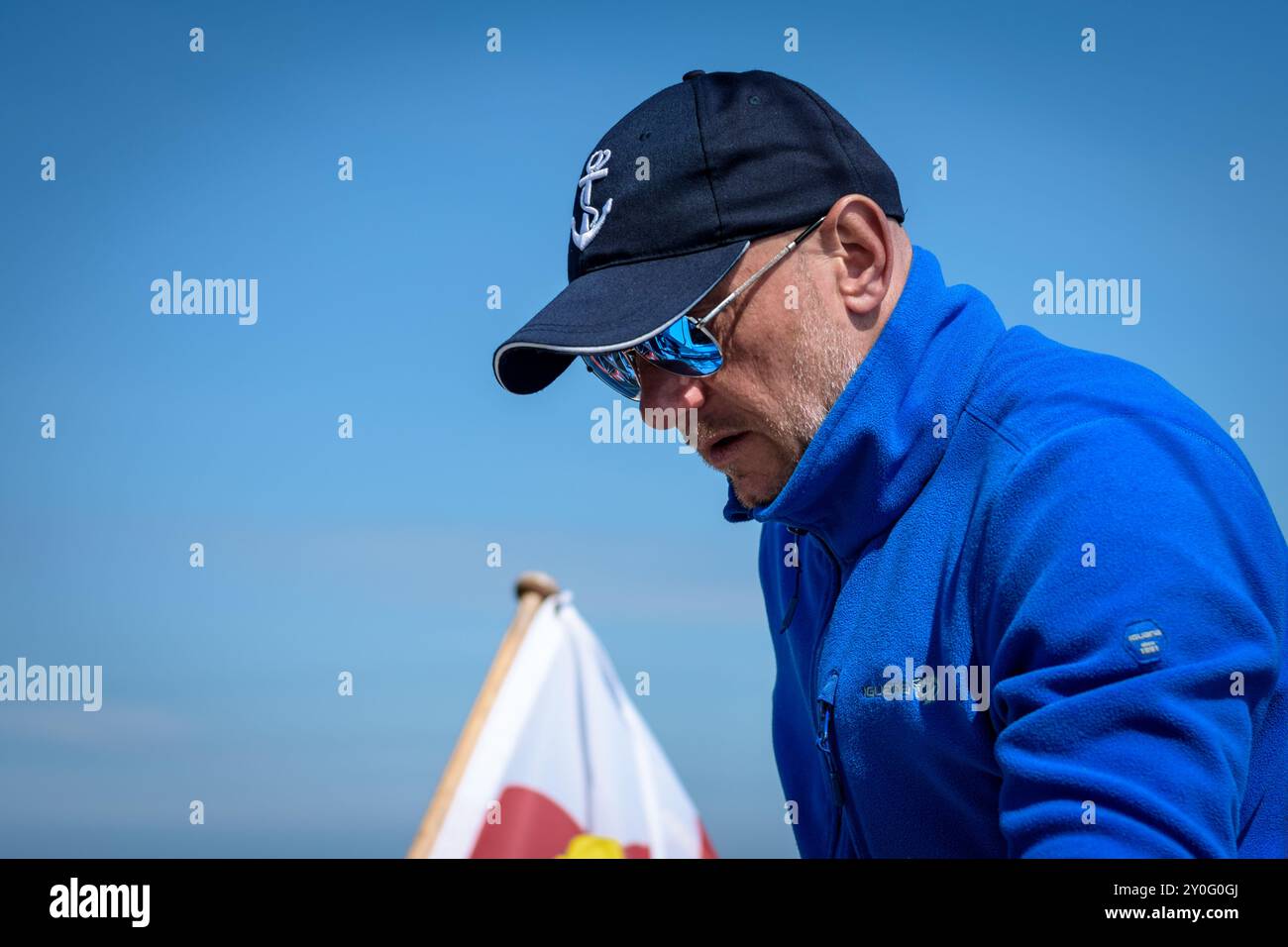 Nahaufnahme eines Mannes im nautischen Stil mittleren Alters mit Spiegelbrille, der ein blaues Fleece-Sweatshirt und eine Baseballmütze trägt Stockfoto