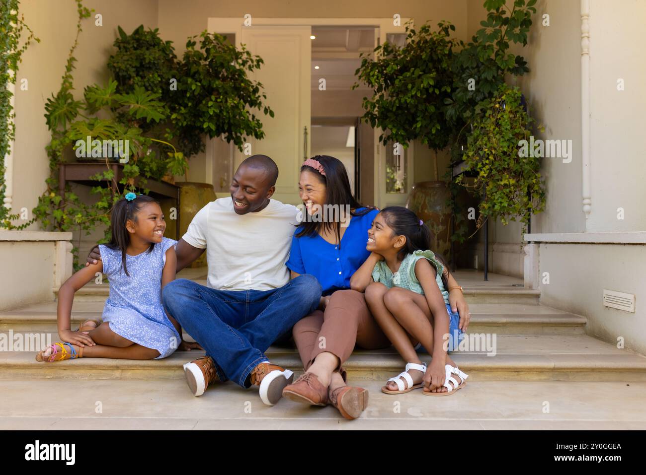 Auf Stufen sitzend, glückliche vierköpfige Familie mit Töchtern, die die gemeinsame Zeit zu Hause genießen Stockfoto