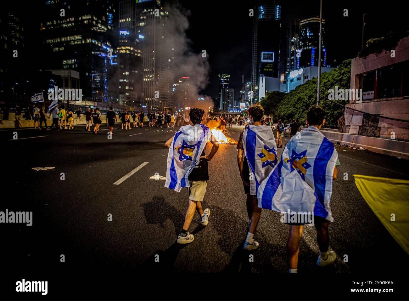 Israelische Demonstranten, die in die israelische Flagge gehüllt wurden, gehen während der Demonstration zu einem Lagerfeuer entlang des Ayalon-Highways. Die Organisatoren behaupten, dass sonntagabends über 700.000 Israelis in Städten im ganzen Land auf die Straßen gedrungen sind, nachdem die Leichen von Karmel Gat, Eden Yerushalmi, Hersh Goldberg-Polin, Alexander Lobanov, Almog Sarusi und Meister Sgt Ori Danino aus Gaza gerettet wurden. Demonstranten forderten, dass Premierminister Benjamin Netanjahu einen Waffenstillstand mit der Hamas eingeht, um die verbliebenen Gefangenen nach Hause zu bringen. Stockfoto