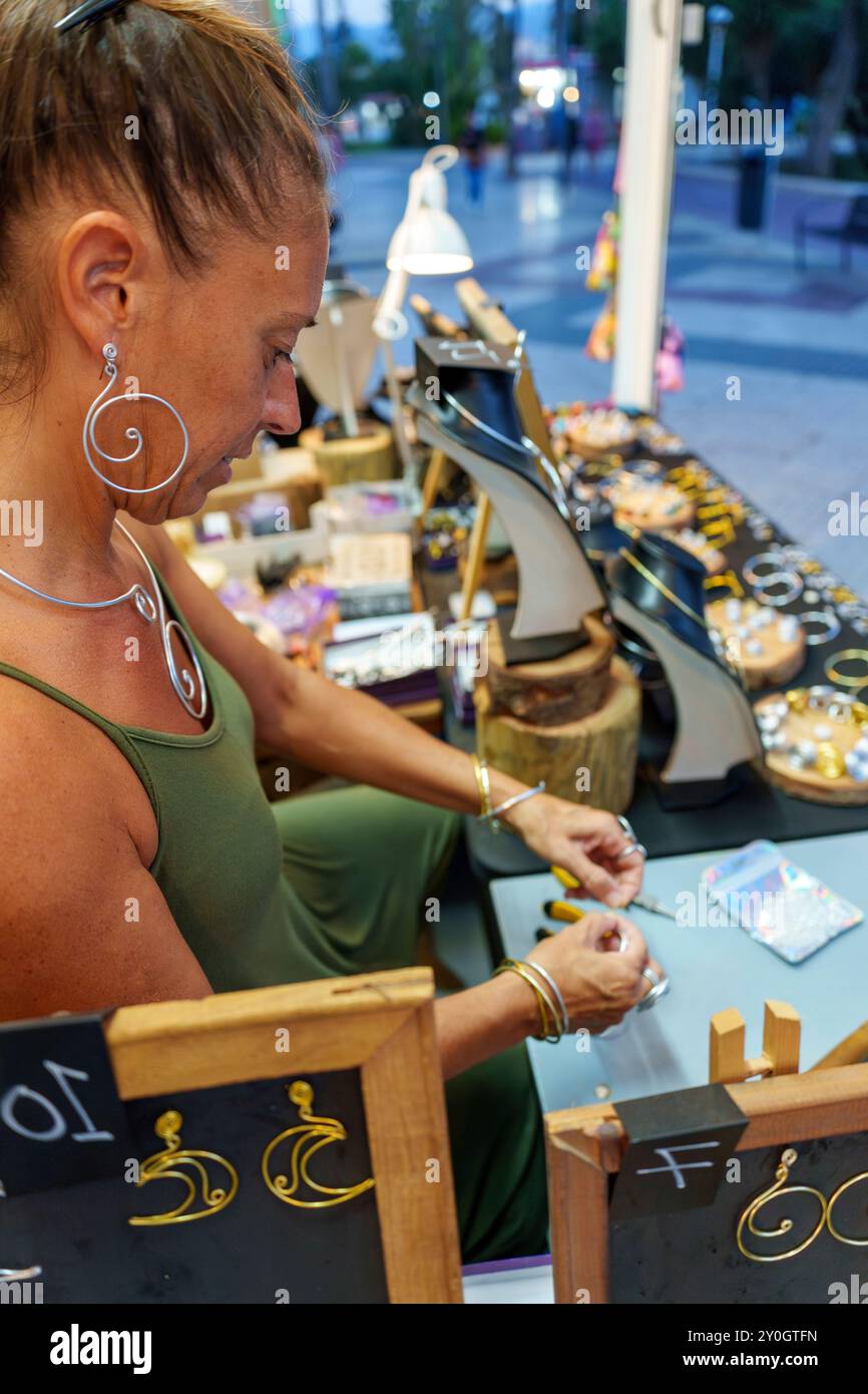 Hispanische Frau in ihren 50ern, die Ohrringe an ihrem Straßenstand herstellt und handgefertigten Aluminiumdrahtschmuck verkauft Stockfoto