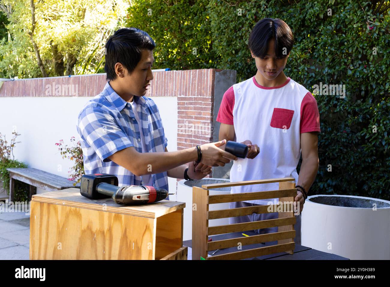 Asiatischer Vater und Sohn im Teenageralter bauen eine Holzkiste in einem Außenarbeitsbereich zusammen Stockfoto