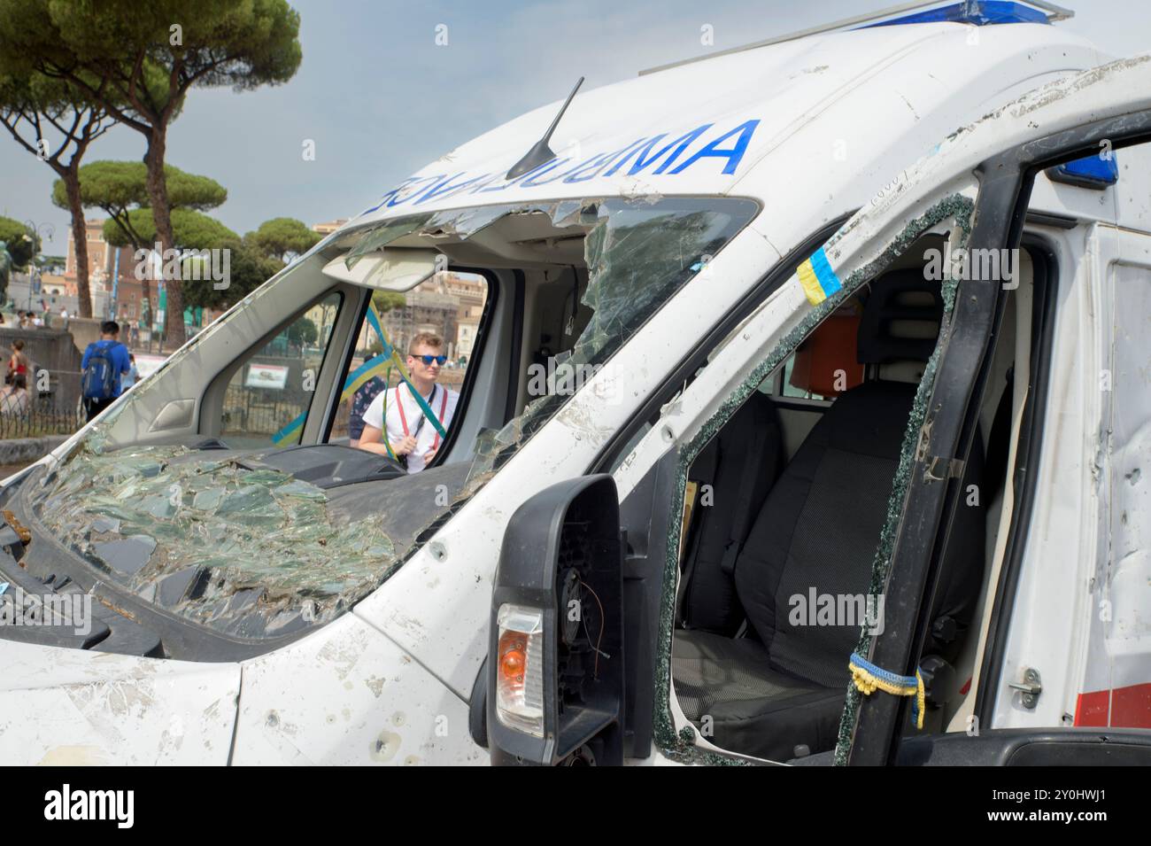 Rom, Italien. September 2024. Ein Tourist betrachtet den von russischer Artillerie in der Region Charkiw zerstörten Krankenwagen, der für die Kampagne 'Ukraine ruft' von der Organisation LUkraine in Zusammenarbeit mit der christlichen Vereinigung der Ukrainer in Italien in Rom ausgestellt wurde. Ebenfalls in Rom ist ein Krankenwagen aus der russisch-ukrainischen Kriegszone zu sehen, der für die Kampagne 'Ukraine is Calling', die von der luxemburgischen gemeinnützigen Organisation LUkraine gestartet wurde, durch Europa bereist. Ziel ist es, Mittel für den Kauf von 112 Krankenwagen und Feuerwehrfahrzeugen für die Frontlinien zu sammeln. Nach Angaben der Organisatoren in SE Stockfoto