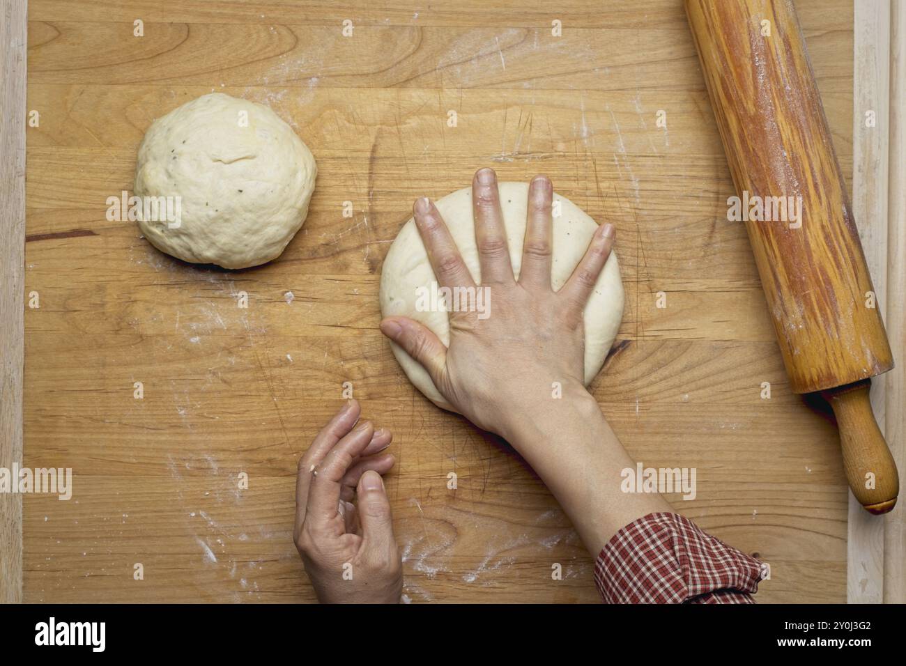 Ein flaches Foto, auf dem eine kleine Kugel Teig hinunterklopft wird, damit sie mit dem Nudelstift ausgerollt werden kann Stockfoto