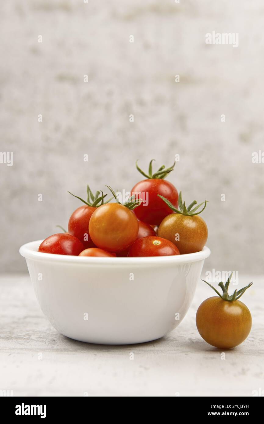 Ein Studiofoto von frischen Reifen Kirschtomaten in einer weißen Schüssel mit einer Tomate an der Seite Stockfoto