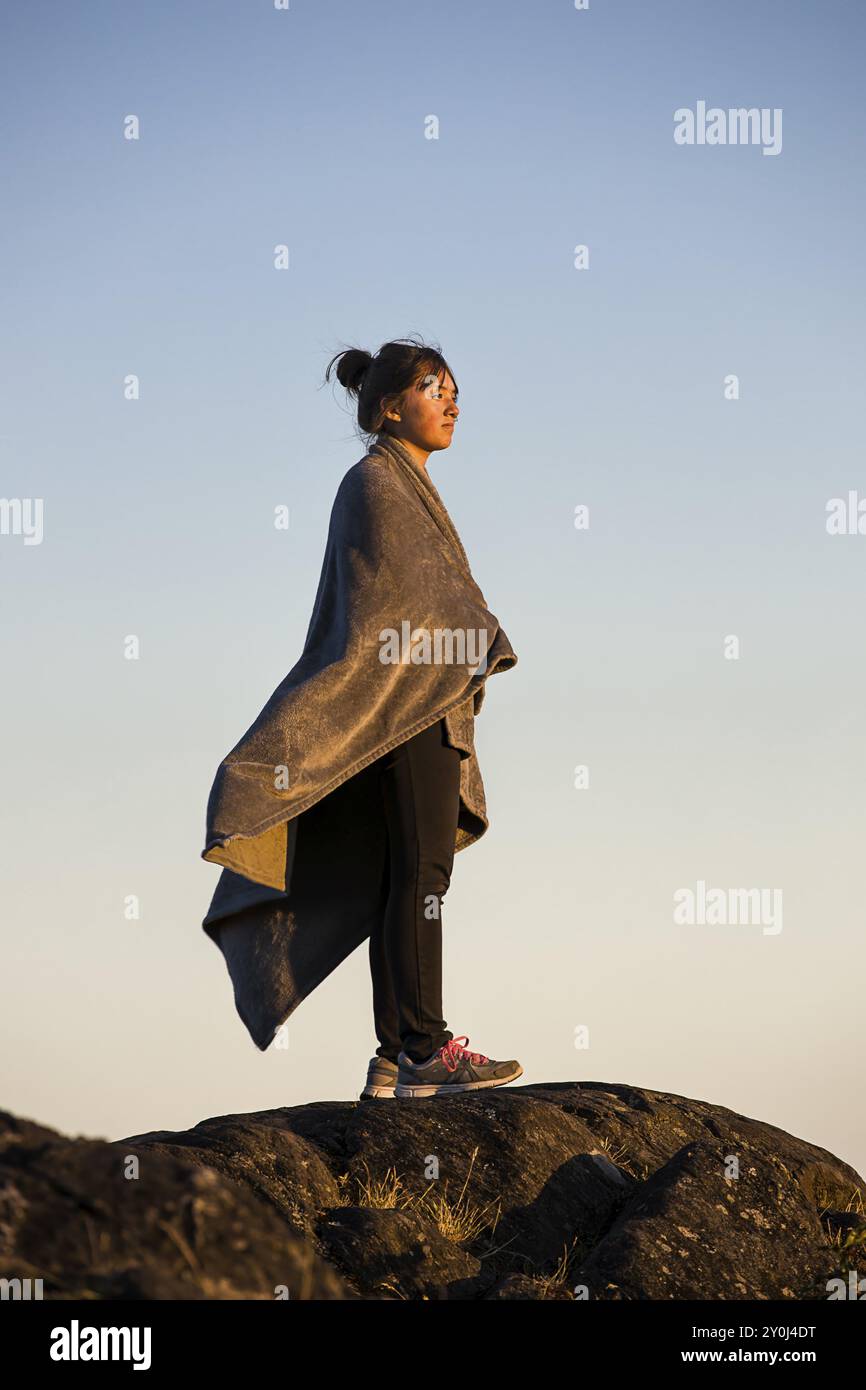 Ein Teenager-Mädchen ist in eine Decke gewickelt und beobachtet den Sonnenuntergang in Anacortes, Washington Stockfoto