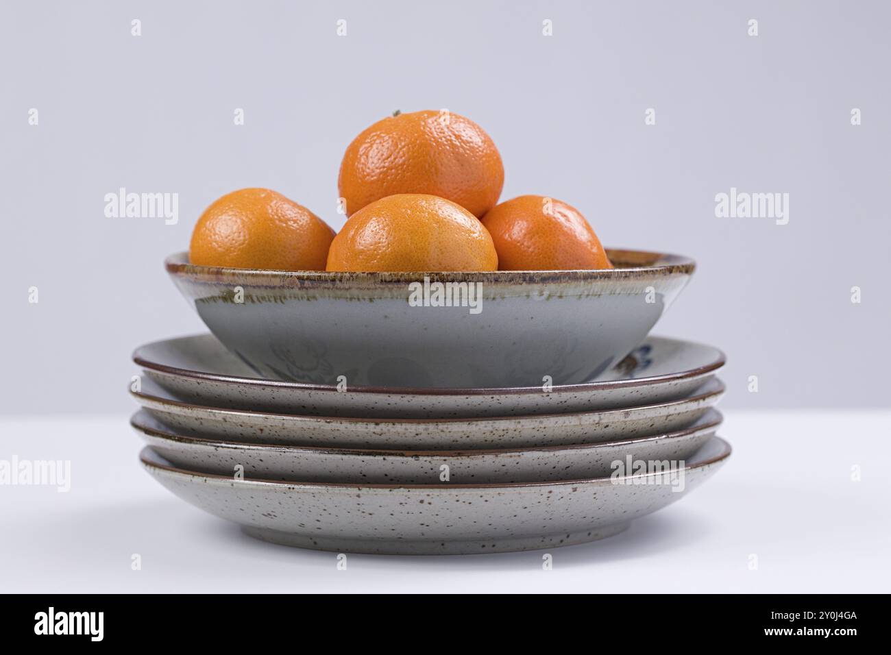 Ein Studio-Foto von kleinen süßen Orangen in einer Schüssel auf gestapelten Tellern Stockfoto