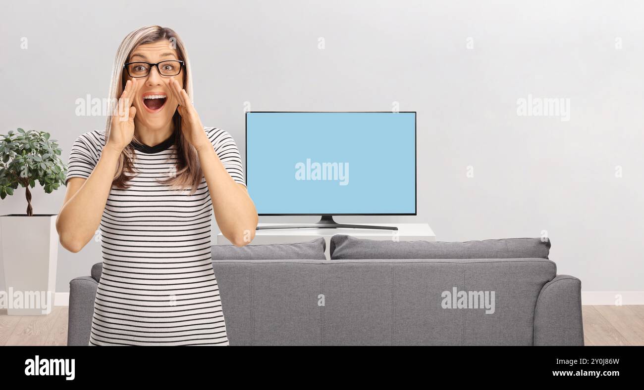 Blonde Frau mit Brille, die zu Hause vor dem fernseher schreit Stockfoto