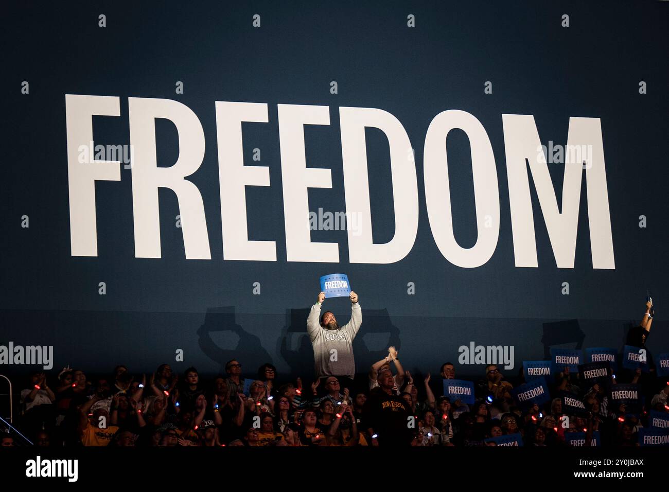 Ein Zuschauermitglied hält ein „FREIHEIT“-Zeichen über seinem Kopf vor einem großen „FREIHEIT“-Banner bei einer Harris/Walz-Wahlkampfveranstaltung. Stockfoto