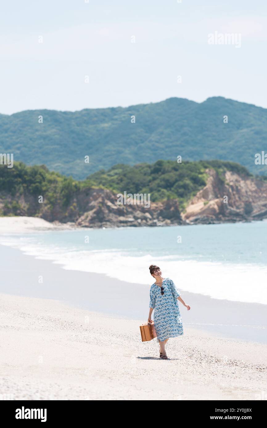 Frau, die mit einer Reisetasche am Strand läuft Stockfoto