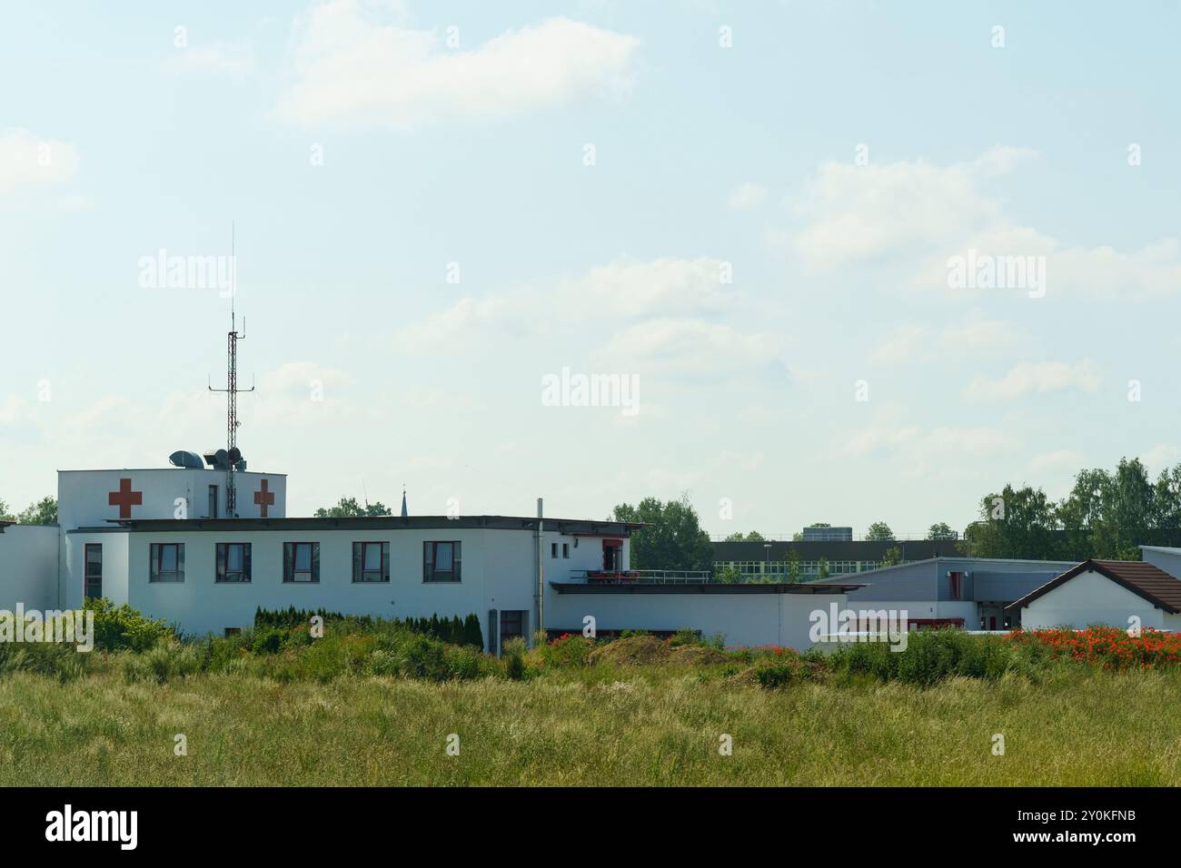 Die beschauliche Szene fängt eine medizinische Einrichtung ein, die inmitten von üppigem Grün liegt, mit einem leuchtend blauen Himmel darüber und sanften Wolken, die an eine se erinnern Stockfoto