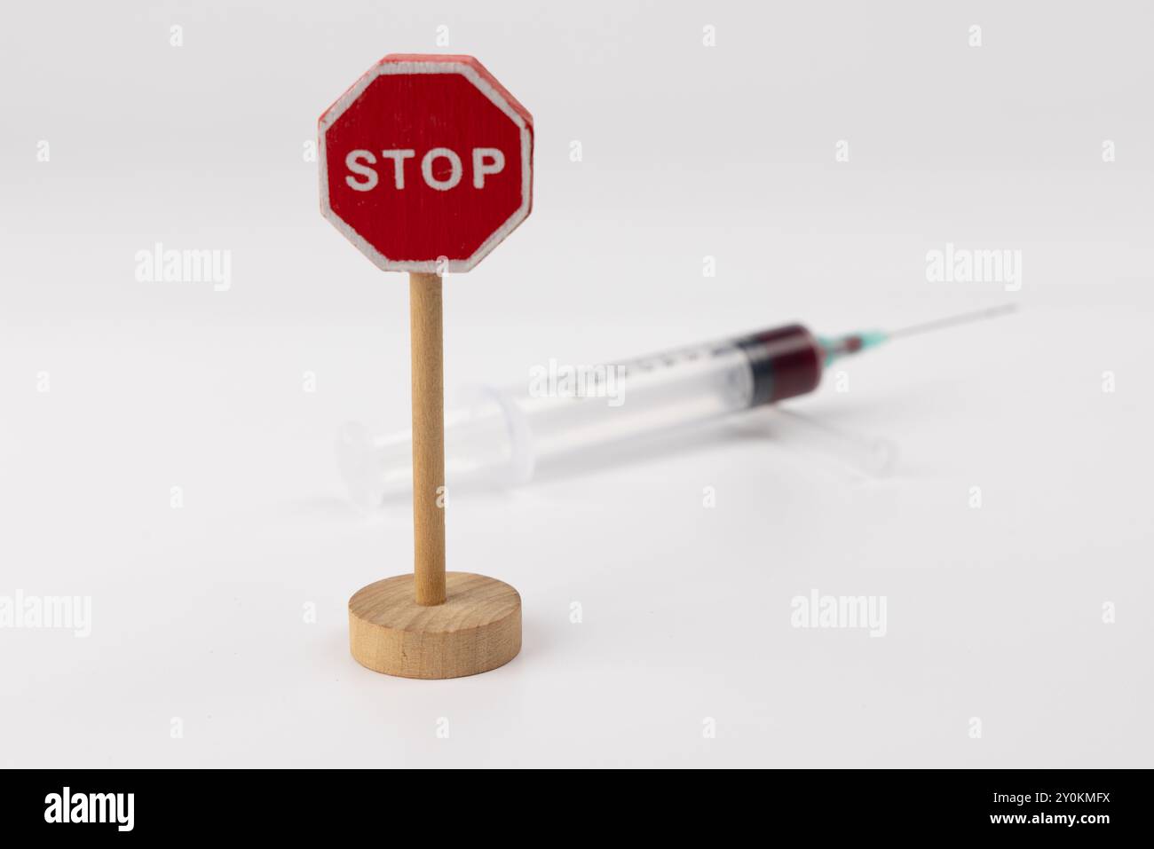 Detaillierte horizontale Aufnahme mit einem hölzernen Stoppschild und einer mit Blut gefüllten Spritze in der Mitte. Der weiße Hintergrund sorgt für einen klaren Ko Stockfoto