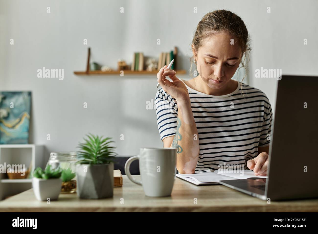 Eine nachdenkliche Frau mit Vitiligo schreibt, umgeben von Pflanzen und einem warmen Ambiente. Stockfoto