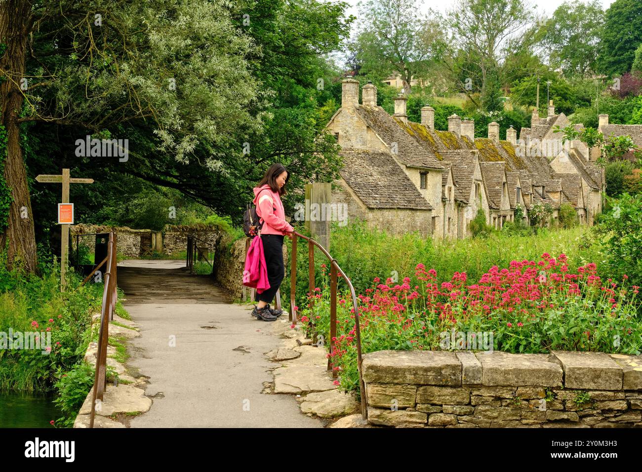 Tourist auf Steinbrücke Fußweg in Richtung der malerischen Arlington Row Weavers Cottages, Bibury, Cotswolds, England, Großbritannien Stockfoto