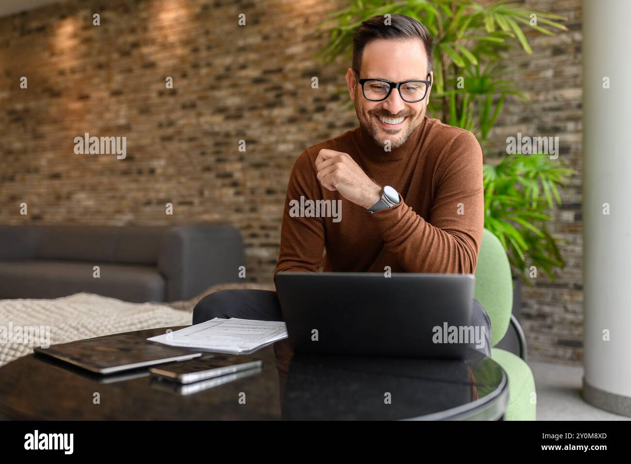 Porträt eines gutaussehenden Ingenieurs, der am Projekt über einem Laptop arbeitet, während er im modernen Büro am Tisch sitzt Stockfoto