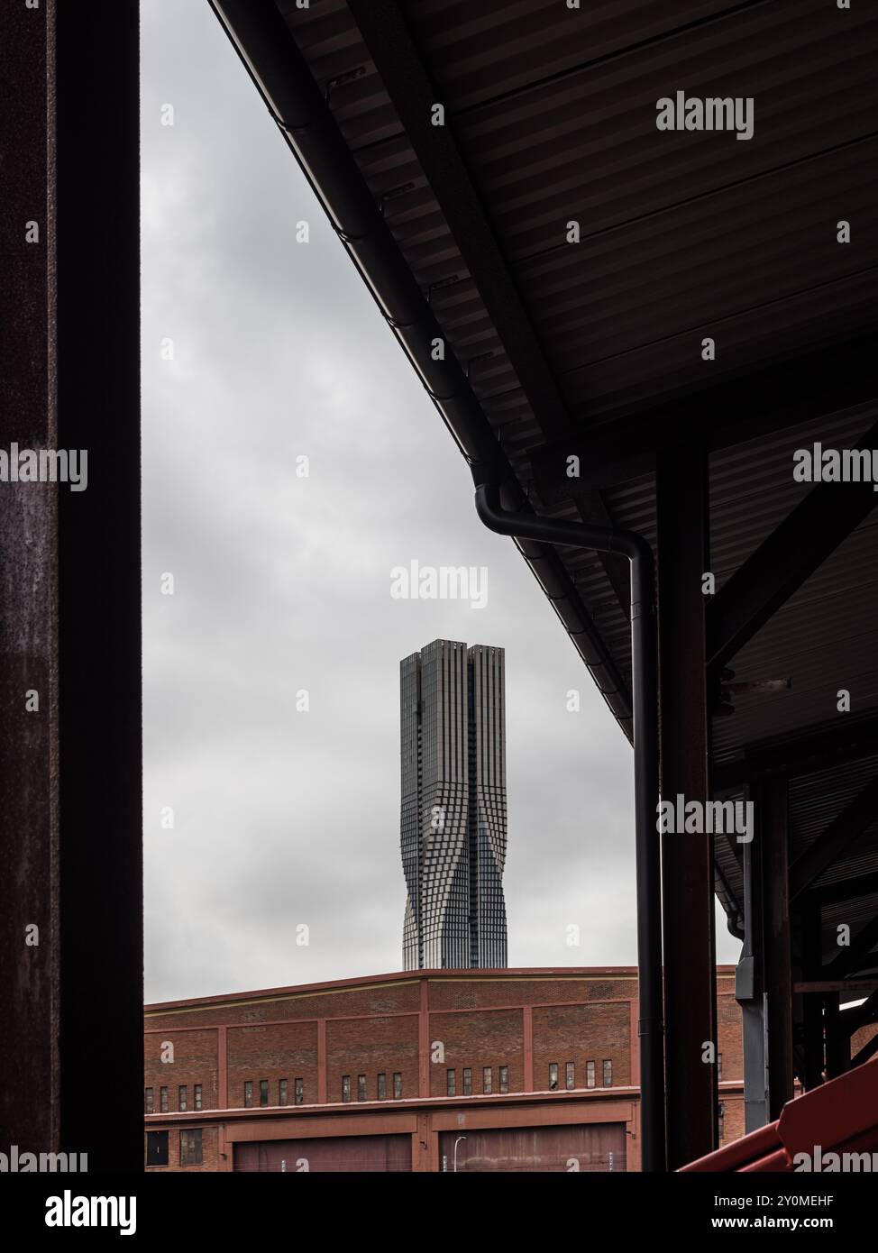 Ein markanter Wolkenkratzer erhebt sich in Göteborg über Industriegebäuden und zeigt moderne Architektur vor einem grauen, bewölkten Himmel. Stockfoto