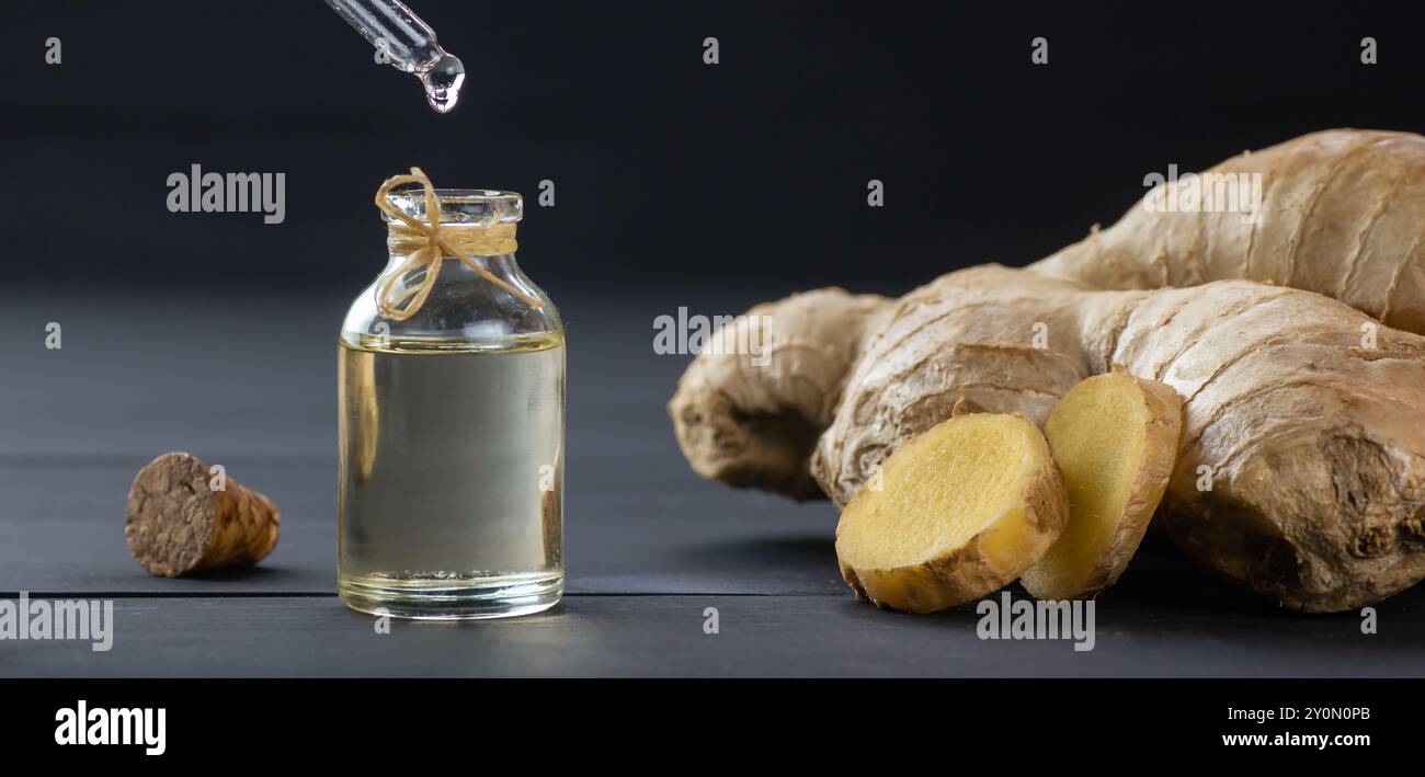 Glasflasche mit ätherischem Ingweröl, Ingwerwurzel und Pulver auf schwarzem hölzernen rustikalen Hintergrund, Öl tropfend, Zingiber officinale Stockfoto