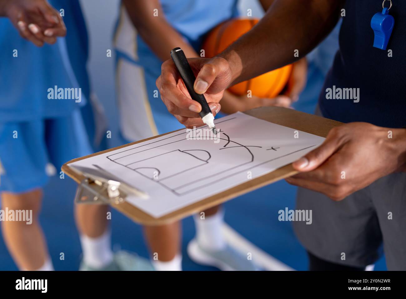 Männliche Trainer zeichnen Basketball spielen auf dem Klemmbrett, die Spieler hören aufmerksam im Fitnessstudio zu Stockfoto