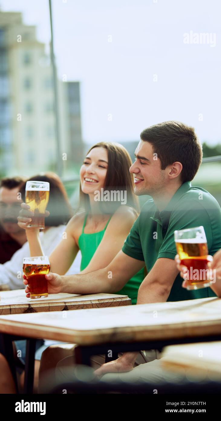 Junger bärtiger Mann genießt kaltes Bier in entspannter Atmosphäre im Freien und genießt Momente. Frau sitzt in der Nähe. Festliche Atmosphäre. Stockfoto