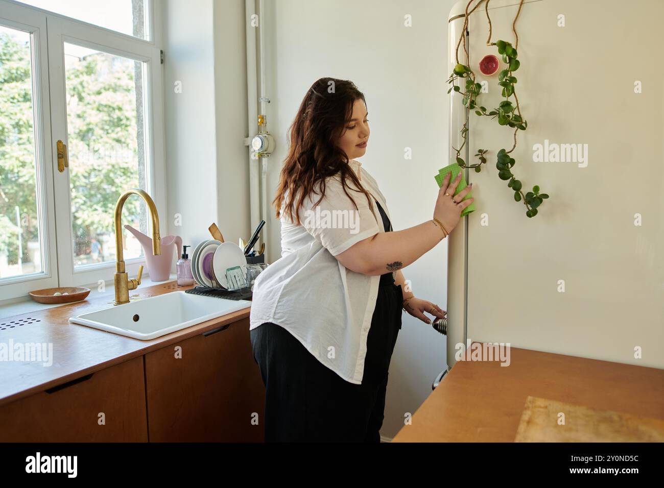 Frau genießt es, die Küche aufzuräumen, während sie von natürlichem Licht umgeben ist. Stockfoto