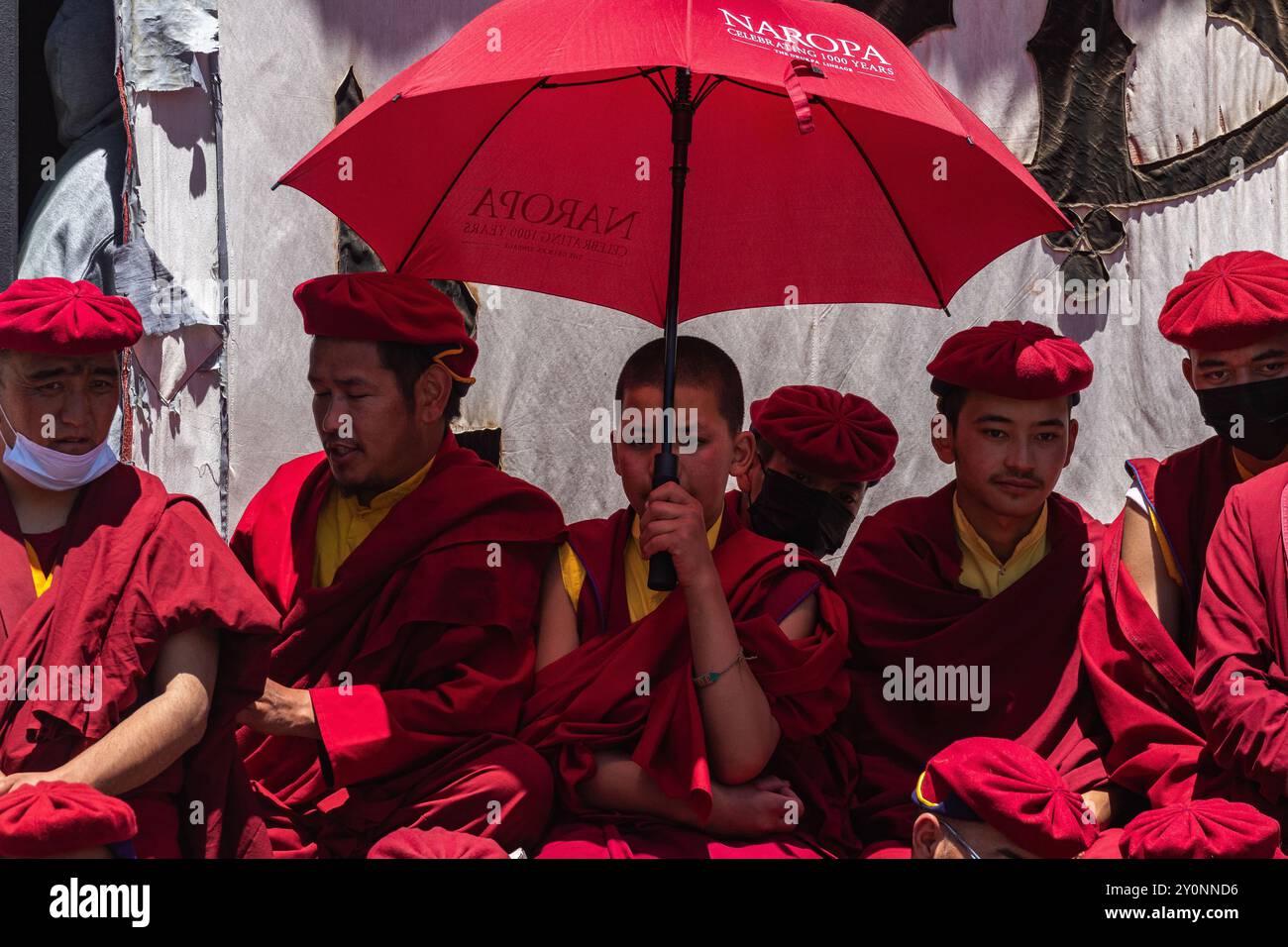Tibetische Mönche, die rote Gewänder tragen und einen Regenschirm benutzen, sitzen am 5. Juli 2024 in Leh, Indien zusammen. Stockfoto