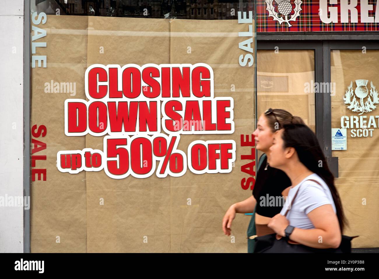 Junge Frau (mit Bewegungsunschärfe), die an einem Verkaufsschild an einem Schaufenster in der Princes Street, Edinburgh, Schottland, Großbritannien vorbeiläuft. Stockfoto