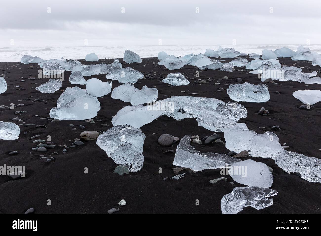 Diamond Beach in Island – transparente Eisberge, die an Land gewaschen werden, auf schwarzem Sandstrand mit Meereslandschaft im Hintergrund. Stockfoto