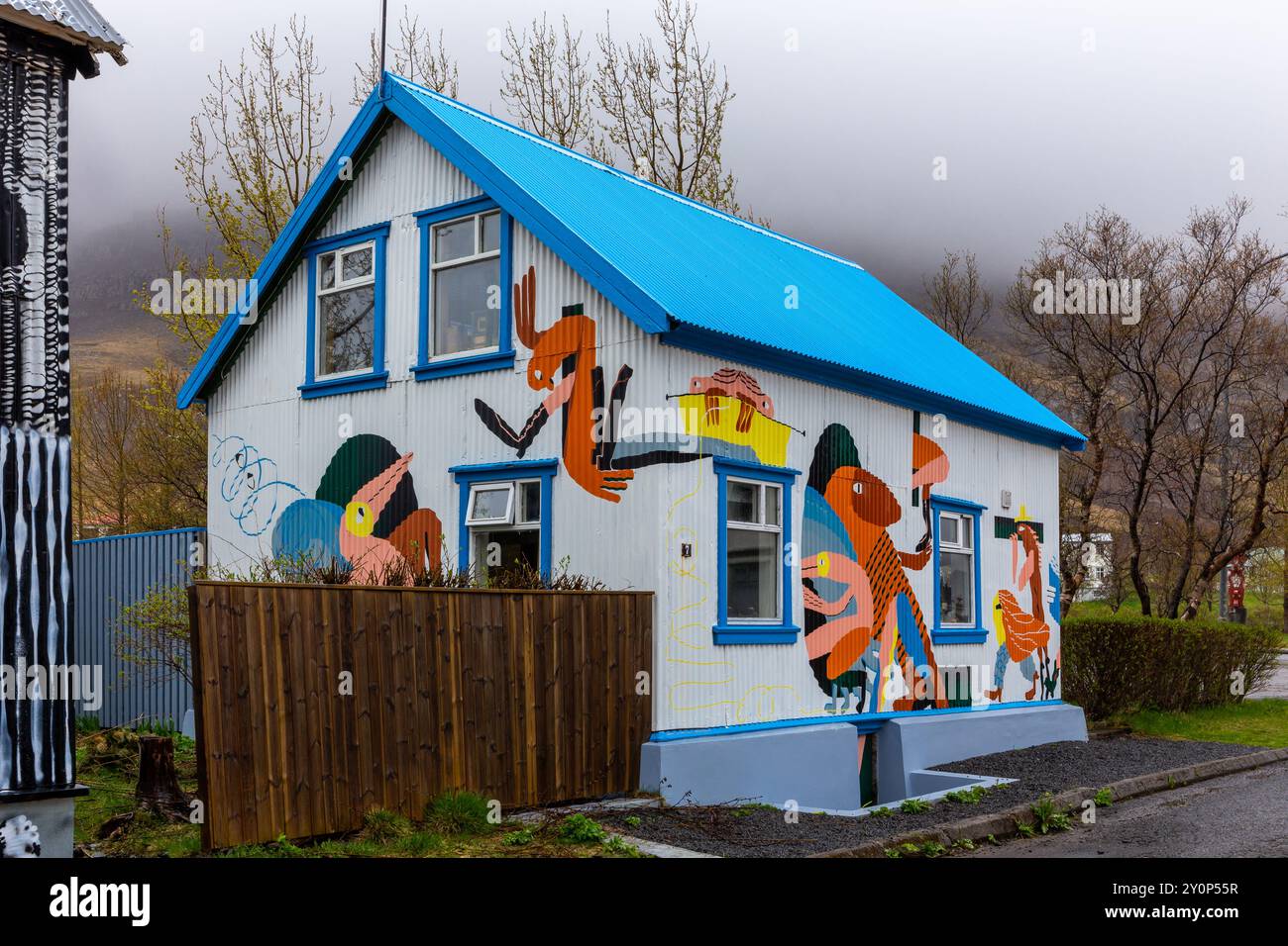 Seydisfjordur, Island, 19.05.2022. Traditionelles isländisches Haus in Seydisfjordur mit farbenfrohen Gemälden und nebeligen Bergen im Hintergrund. Stockfoto