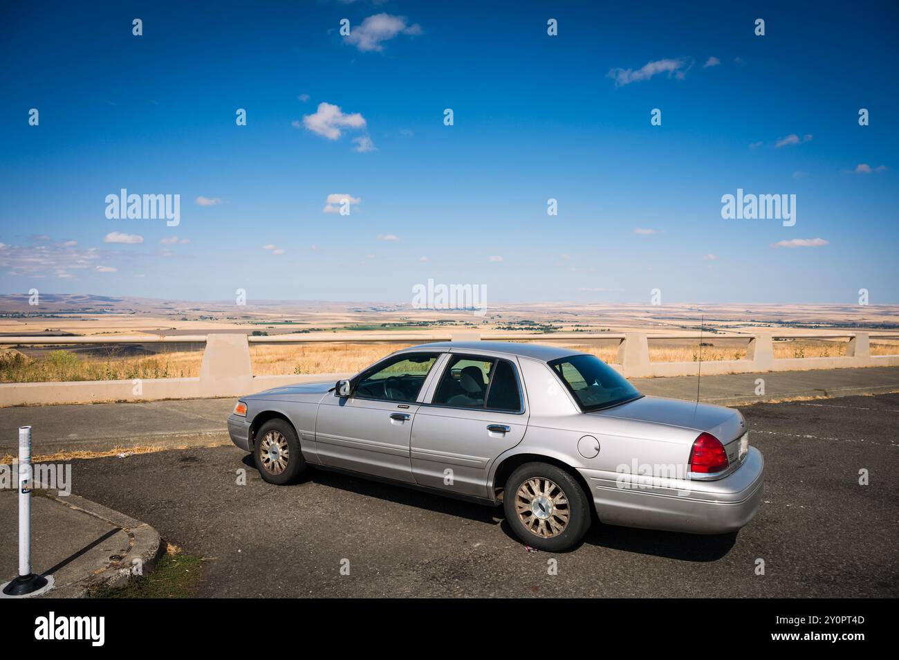 Eine Frau blickt von einer Raststätte auf die Prärie von Oregon und das Land. Gelbe Weizenfelder, blauer Himmel und ein blaues Kleid. Ford Crown Victoria Stockfoto