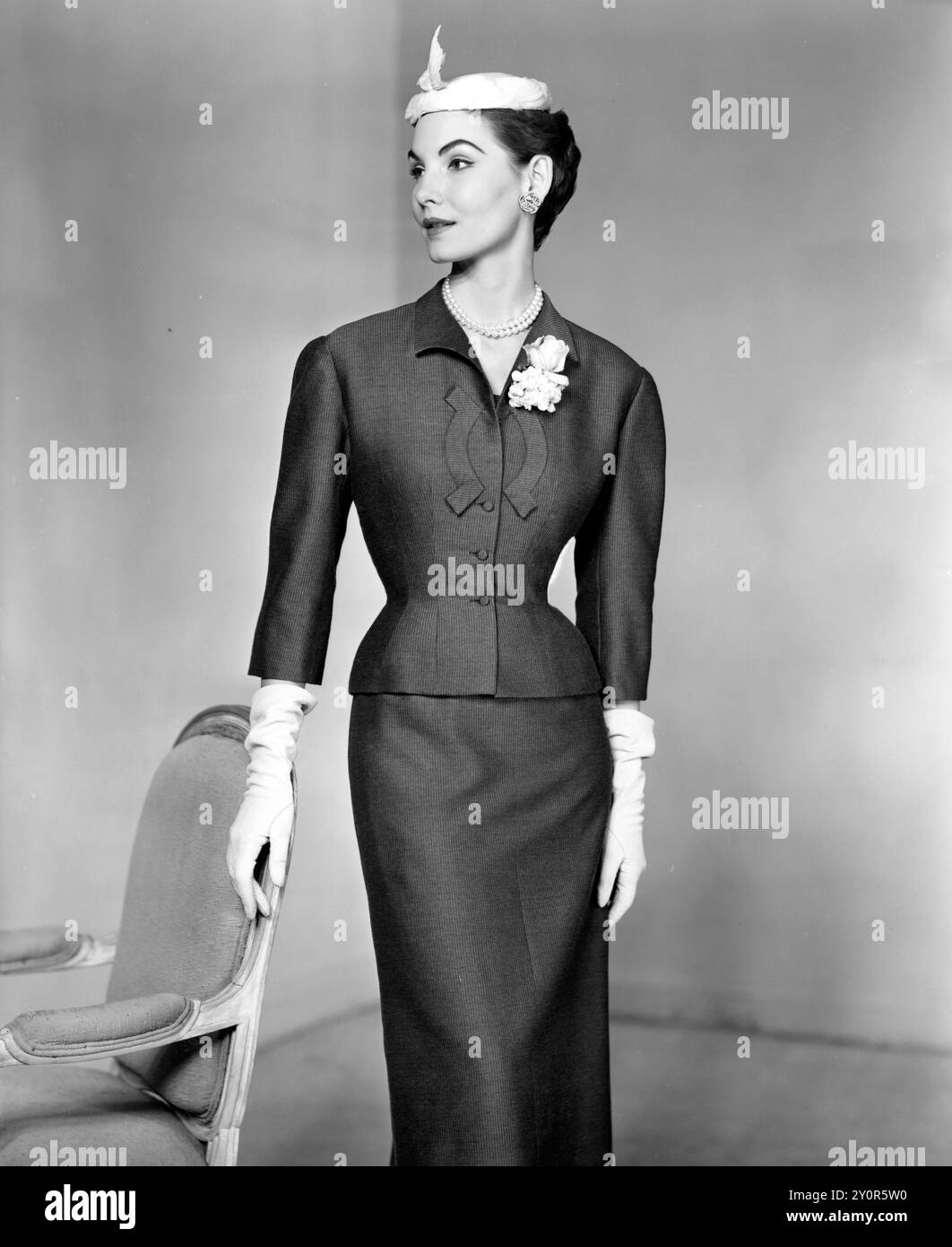 15. Januar 1954: New York, New York, Vereinigte Staaten: Hattie Carnegies dunkelgraues ärmelloses Kleid und Jackenkostüm aus gestreiftem Doeskin, entworfen für Frühjahr 1854. Das Kleid mit Prinzessin-Linie hat einen niedrigen, rechteckigen Ausschnitt, der durch eine vornehme Biegung des Stoffes vervollständigt wird. Die Jacke wird durch eine Sticknadel-Corsage aus weißen Veilchen und Rosen aufgehellt. (Foto: © Keystone Press Agency/ZUMA Press Wire). NUR REDAKTIONELLE VERWENDUNG! Nicht für kommerzielle ZWECKE! Stockfoto