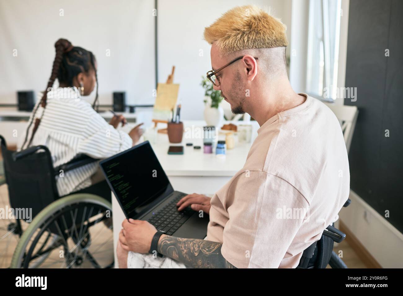 Team von Kollegen, die in modernen, inklusiven Büros mit Laptops und Technologie zusammenarbeiten, Rollstuhlfahrer, die produktive Aufgaben in Freizeitkleidung erledigen Stockfoto