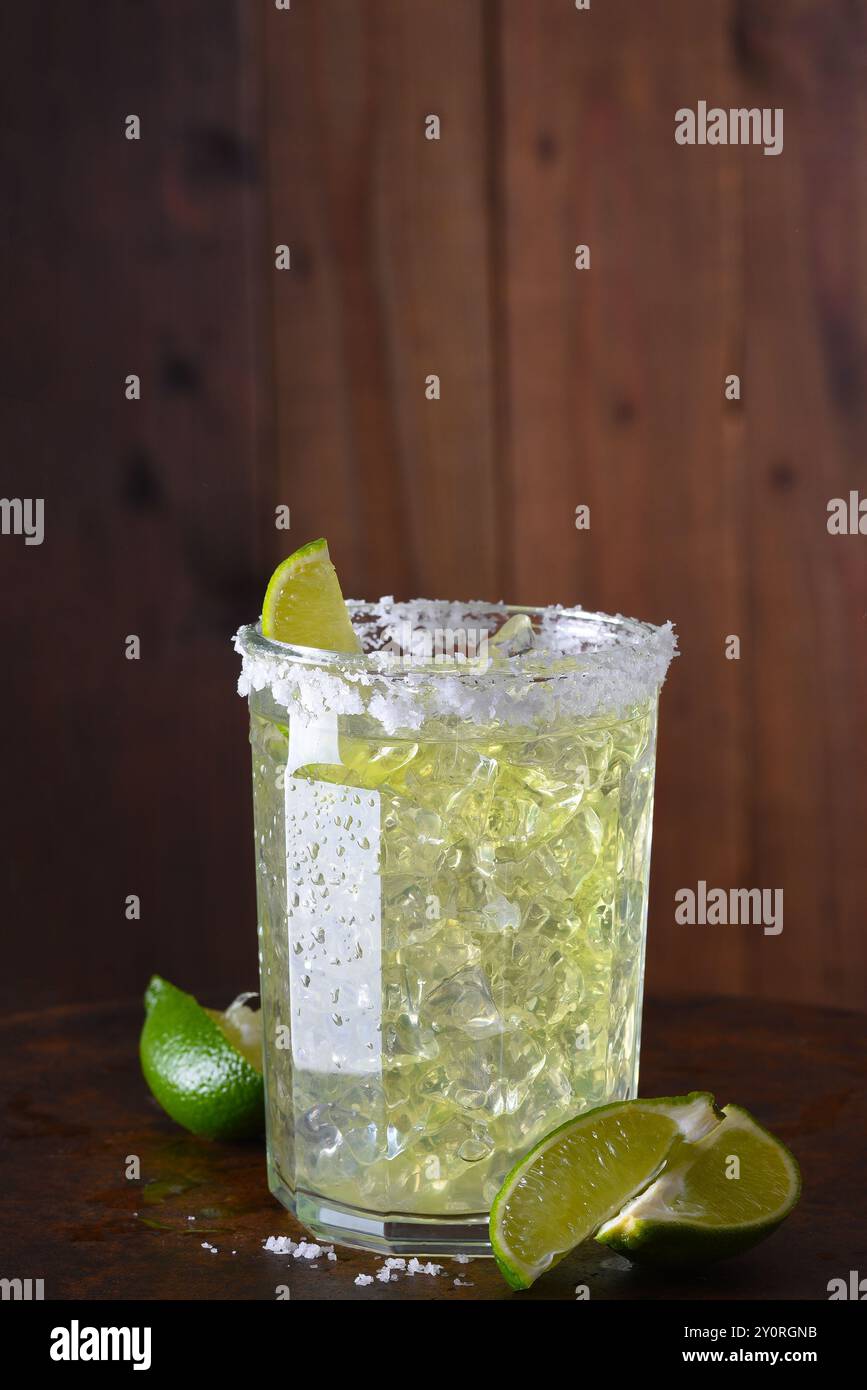 Eine Margarita auf den Felsen in einem Glasbecher. Der Glasrand ist mit Salz verkrustet, und auf der Stangenoberfläche befinden sich in Scheiben geschnittene Limetten. Stockfoto