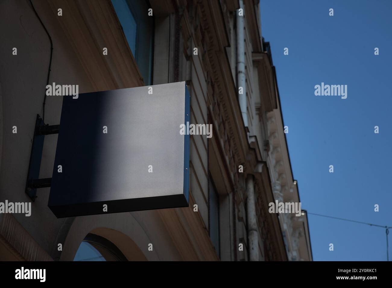 Leere blaue graue quadratische Ladenschilder, die an einer Gebäudefassade hängen und in einer europäischen Stadtstraße vor klarem Himmel sichtbar sind, ideal für Einzelhandelsgeschäfte A Stockfoto