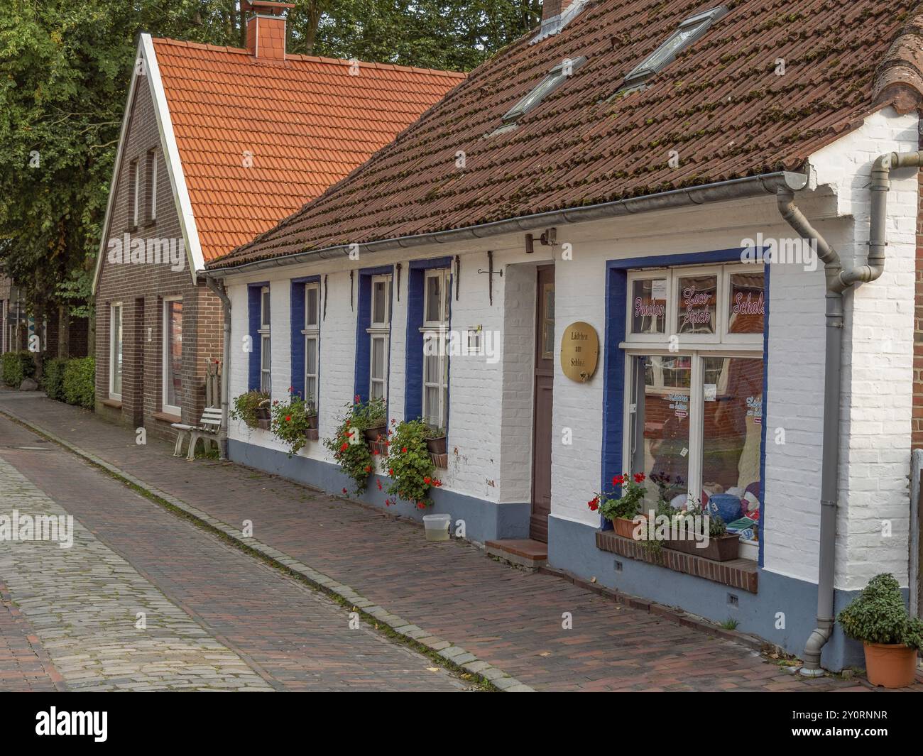 Reihenhäuser mit Ziegeldächern und Blumenkästen an den Fenstern, Kopfsteinpflasterstraße, dornum, ostfriesland, deutschland Stockfoto