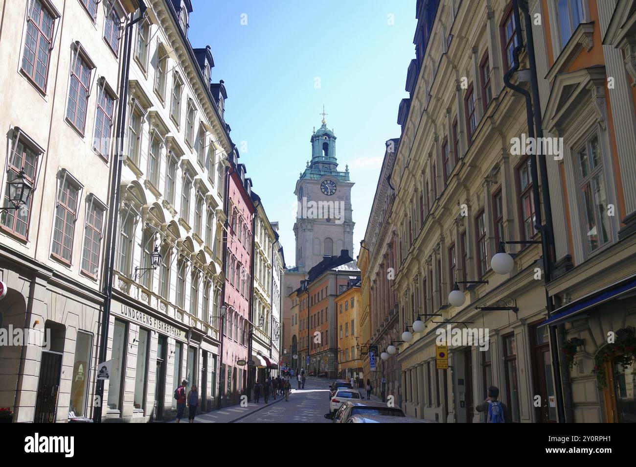 Enge Straße zwischen hohen, pastellfarbenen Gebäuden mit Blick auf einen Kirchturm an einem sonnigen Tag, Gamla Stan, Altstadt, Stockholm, Schweden, Europa Stockfoto