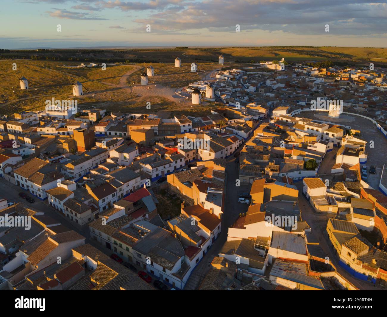 Dächer und Häuser eines Dorfes in der Abenddämmerung mit Windmühlen im Hintergrund und orangefarbener Beleuchtung, Luftaufnahme, Windmühlen, Campo de Criptana, Ciudad Real pro Stockfoto