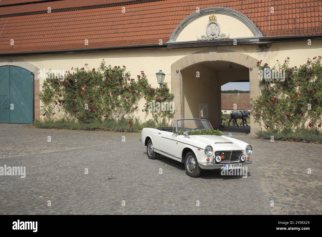 Historisches weißes Fiat Cabrio im Innenhof mit Bogengang, Pflanzenwuchs, Rosen, Rosenhecke, nostalgisch, Idylle, Schloss Fasanerie, Eichenzell, Hessen Stockfoto