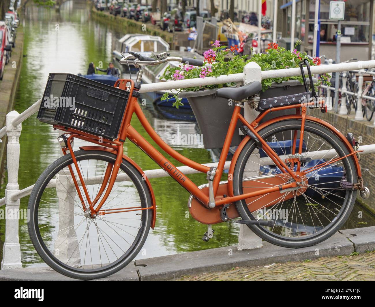 Oranges Fahrrad auf Brücke über Kanal, mit Blumenkorb, städtische Umgebung, delft, niederlande Stockfoto