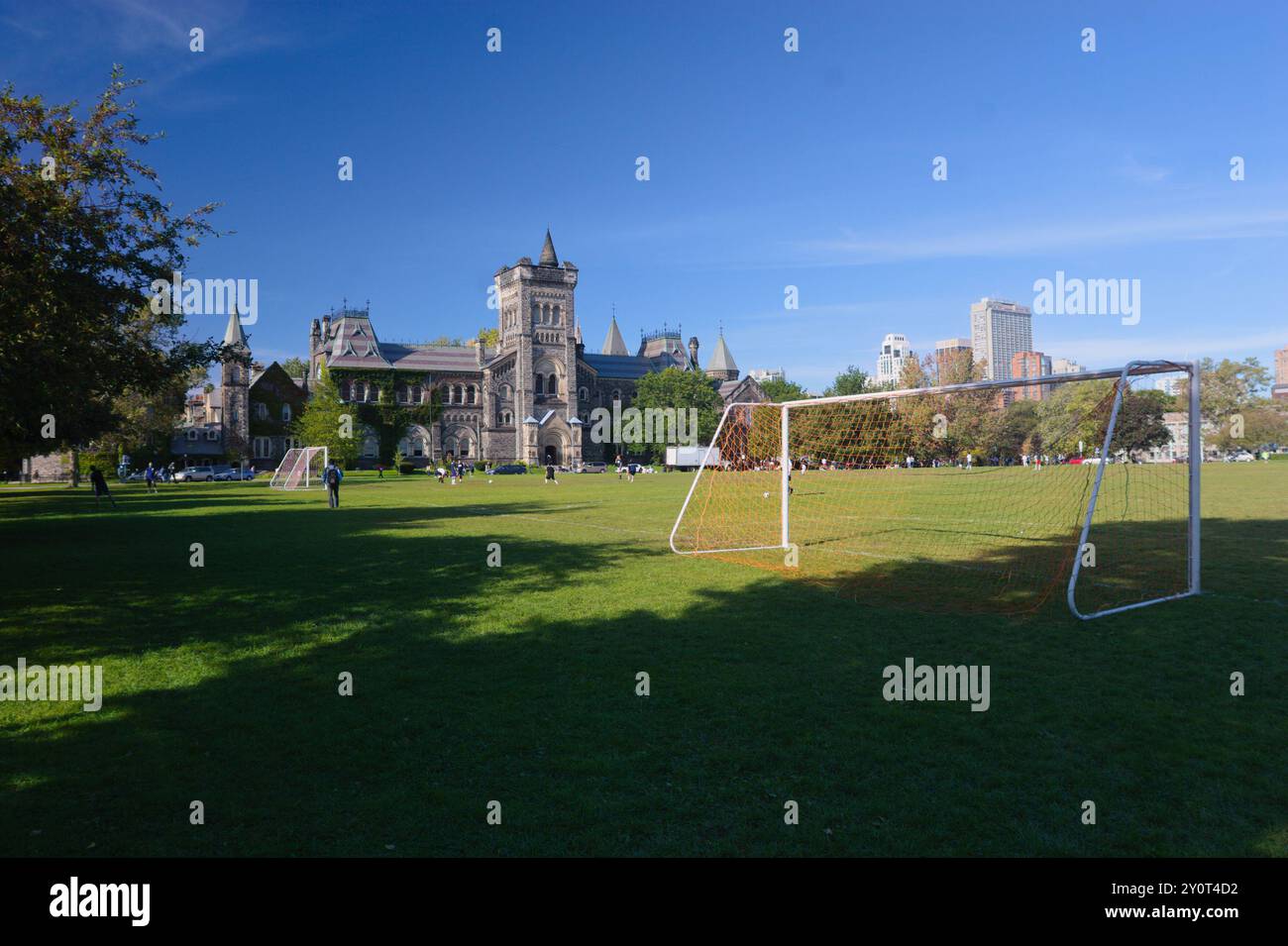 Ein heller, sonniger Tag auf einem grünen Fußballfeld in der Nähe historischer Gebäude, bei dem Spieler ein Spiel genießen und die Wolkenkratzer im Hintergrund sehen. Stockfoto