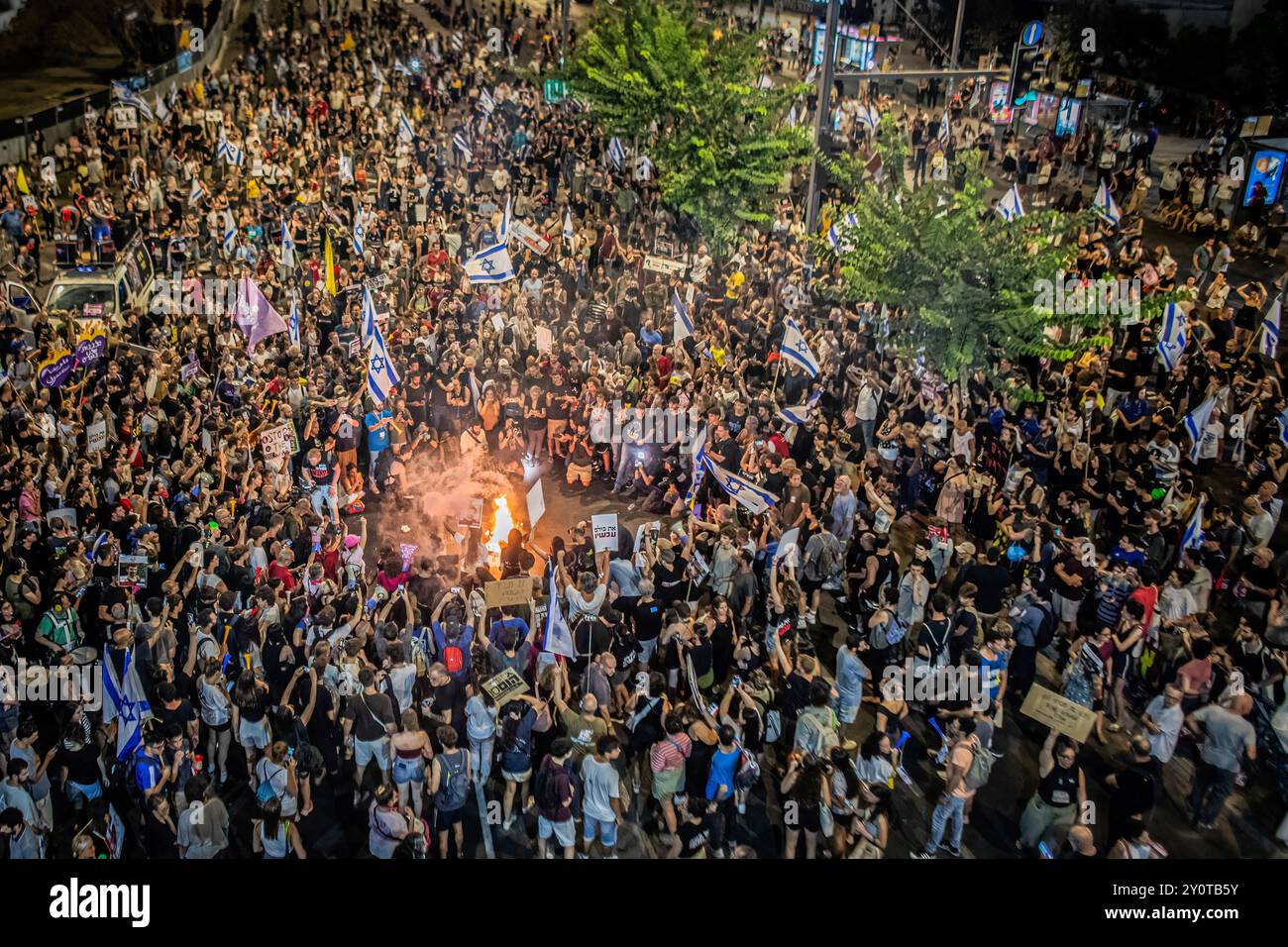 Israelische Demonstranten schwenken ihre Nationalflaggen um ein Lagerfeuer, während einer Demonstration vor dem Verteidigungsministerium. Tausende von Menschen haben sich in Tel Aviv und in ganz Israel versammelt, drei Tage nachdem die Leichen von Karmel Gat, Eden Yerushalmi, Hersh Goldberg-Polin, Alexander Lobanov, Almog Sarusi und Meister Sgt Ori Danino aus Gaza gerettet wurden. Die Demonstranten rufen Premierminister Benjamin Netanjahu und seine Regierung auf, eine Einigung zu erzielen, um die Freilassung der verbleibenden Geiseln zu erreichen, die die Hamas während der Angriffe vom 7. Oktober ergriffen hat. Stockfoto