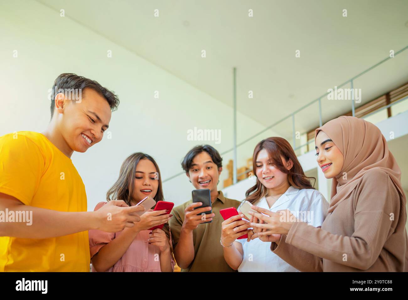 Eine Gruppe indonesischer Menschen steht zusammen und schaut sich ihre Handys an. Sie lächeln alle und scheinen sich zu amüsieren Stockfoto