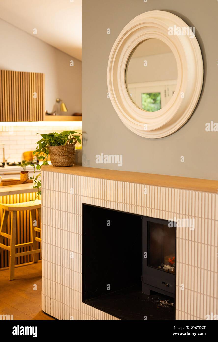 Modernes Wohnzimmer mit Kamin, rundem Spiegel und Topfpflanzen auf Kaminsims, Kopierraum Stockfoto