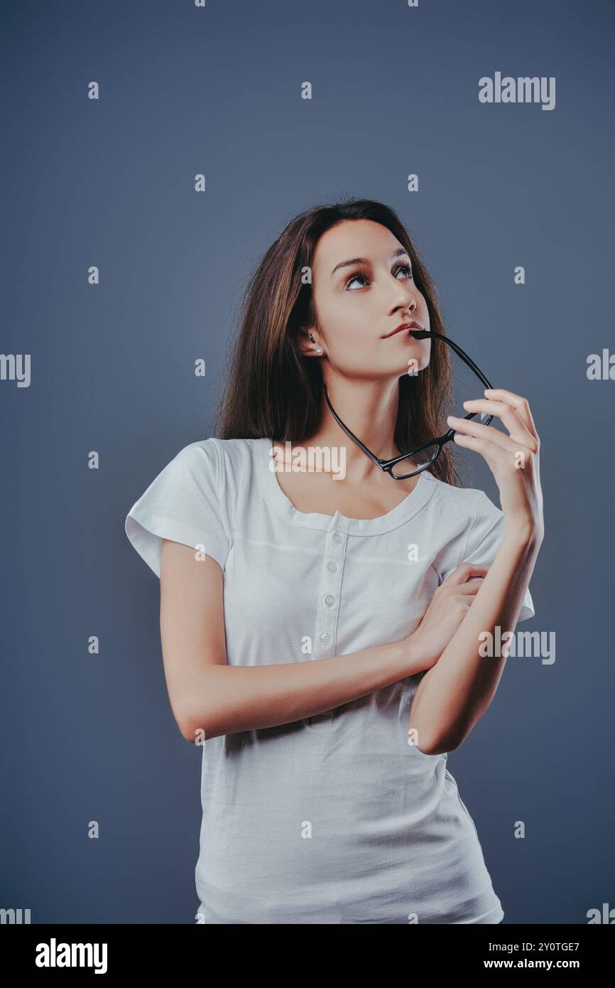Die junge Frau hält ihre Brille, sieht hoffnungsvoll und nachdenklich aus und träumt von ihrer Zukunft. Sie reflektiert und denkt über Lösungen nach, voller Ideen und Rapp Stockfoto
